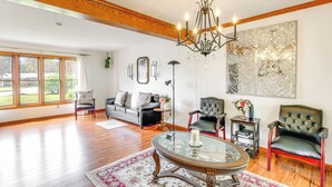 A spacious living room with hardwood floors, a large chandelier, a black leather sofa, a glass coffee table, and a large abstract painting on the wall.