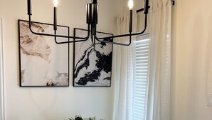 A dining area with a wooden table, four chairs, a chandelier, and two framed artworks on the wall.