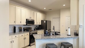 A modern kitchen with white cabinets, stainless steel appliances, granite countertops, and two bar stools.