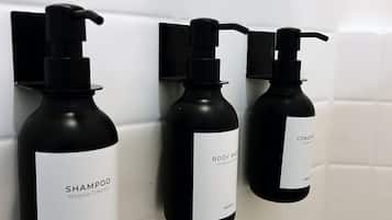 Three black bottles of shampoo and conditioner on a white tiled wall.