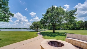 A stone fire pit in a park with a pathway leading to a lake. - Sunrise Cove RC LLC: Lakefront Home w/ 2 Casitas! (Kerens)