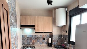 A compact kitchen with wooden cabinets, a gas stove, a built-in oven, a washing machine, and a window with a view.