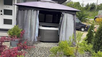 A house with a covered outdoor seating area, a hot tub, and a driveway with gravel and potted plants.
