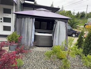 A house with a covered outdoor seating area, a hot tub, and a driveway with gravel and potted plants.