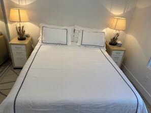A neatly made bed with a white bedspread and two pillows, flanked by two bedside tables with lamps and decorative items.