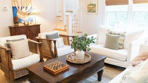 A living room with a sofa, chairs, a coffee table with a chess set, a lamp, and a painting on the wall. - The Long Time PET FRIENDLY Cape Fear Station (bald head island)