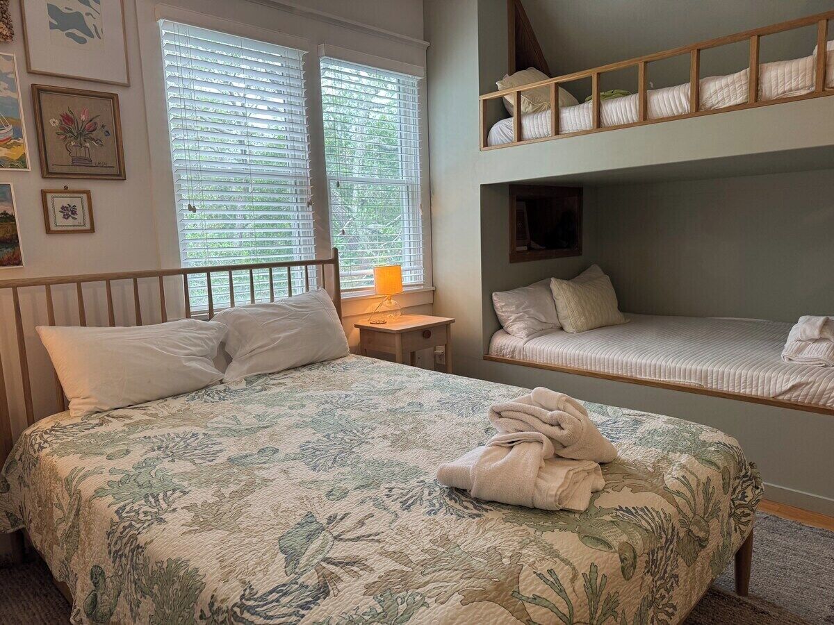 A bedroom with a bed, a bedside table with a lamp, a bunk bed, and framed pictures on the wall.