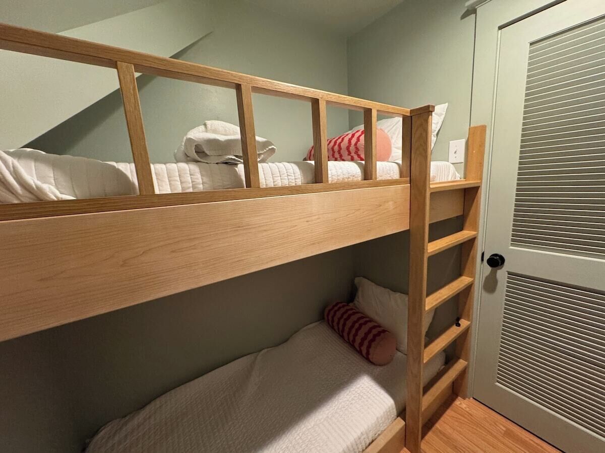 Un lit superposé avec une structure en bois, un lit inférieur avec un oreiller et une porte avec une fenêtre.