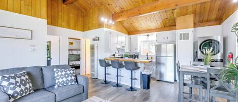 A spacious living area with a grey sofa, a coffee table, and a kitchen in the background.