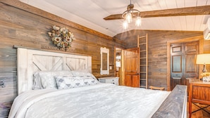 A bedroom with a wooden ceiling, a bed with a white floral bedspread, a dresser, and a mirror.