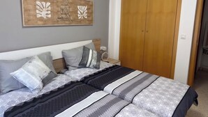 A bedroom with a bed, pillows, a nightstand, a wooden wardrobe, and a wall-mounted artwork. - FIRST LINE BEACH PARTMENT (València)