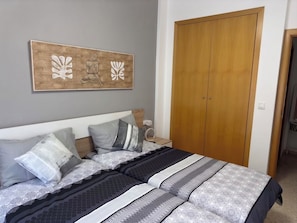A bedroom with a bed, pillows, a nightstand, a wooden wardrobe, and a wall-mounted artwork. - FIRST LINE BEACH PARTMENT (València)