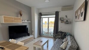 A modern living room with a flat-screen TV, a wooden dining table, a sofa with a patterned cover, and a balcony with a view. - FIRST LINE BEACH PARTMENT (València)