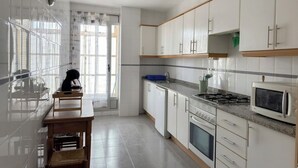 A modern kitchen with white cabinets, a stove, microwave, and a dining area with a table and chairs. - FIRST LINE BEACH PARTMENT (València)