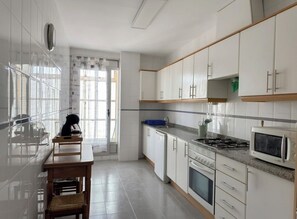 A modern kitchen with white cabinets, a stove, microwave, and a dining area with a table and chairs. - FIRST LINE BEACH PARTMENT (València)
