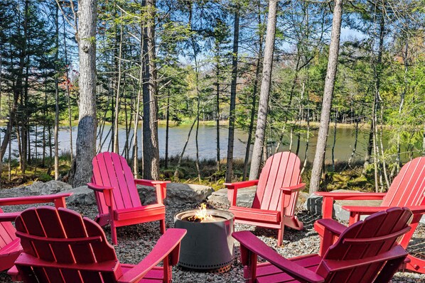 A lakeside seating area with red Adirondack chairs and a fire pit.