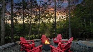A fire pit with four red Adirondack chairs arranged around it, set on a gravel surface in a forested area. - Lakefront luxury,GameRoom,FirePit,Canoe,10Min2JFBB (Blakeslee)