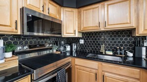 A modern kitchen with wooden cabinets, stainless steel appliances, and a black hexagonal backsplash. - Downtown OC Condo with Bay View, Pool, Parking, Walk to Beach & Boardwalk (Ocean City)