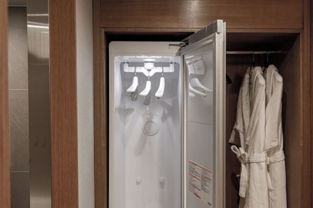 Habitación de hotel con armario de madera, una bata blanca colgada en la puerta y ducha empotrada con panel de control.