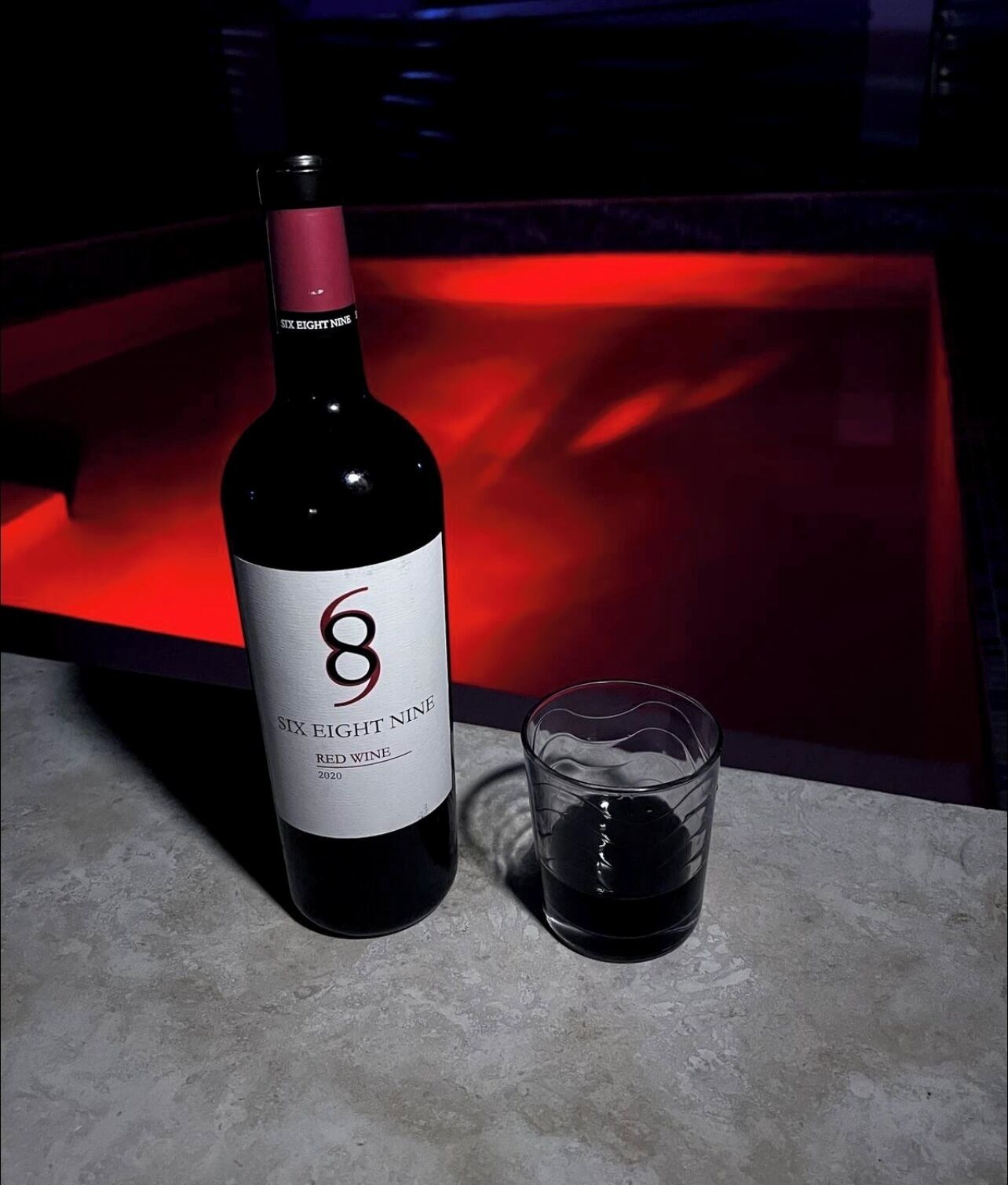 A bottle of Six Eight Nine Red Wine 2020 and a glass of wine on a table.