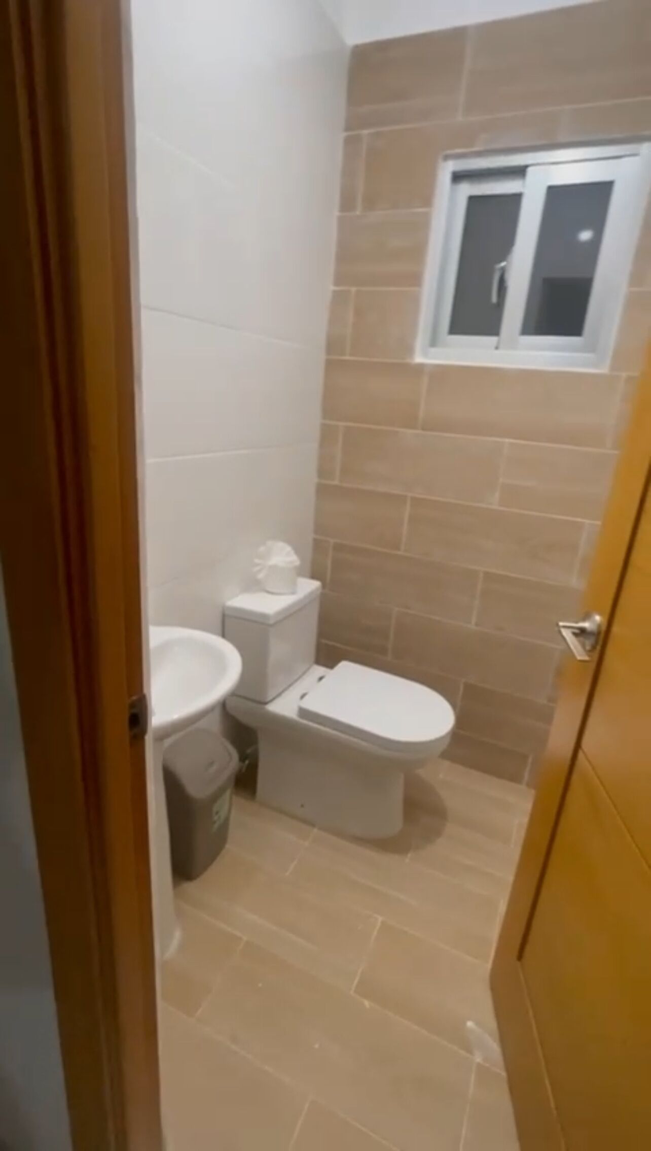 A small bathroom with a toilet, a sink, and a window.