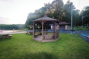 A gazebo with a wooden deck, picnic tables, and a view of a lake.