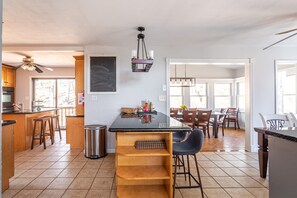 A kitchen with a central island, wooden bar stools, a ceiling fan, and a dining area with a table and chairs.