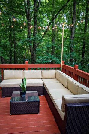 An outdoor deck with a sofa and a table, surrounded by trees and string lights.