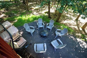 Cadeiras Adirondack dispostas em círculo em torno de uma lareira, em meio à vegetação.