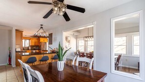 Un comedor amplio con una mesa de madera, sillas blancas y un ventilador de techo.