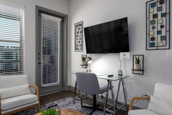 A modern living room with a glass desk, a mounted TV, and two white sofas. - Luxury Apartment: Pool, Near Grandview Medical (Birmingham)