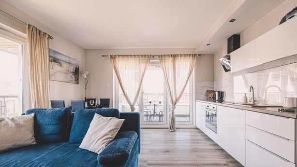 A modern living room with a blue sofa, a dining area, and a kitchen with white cabinets.
