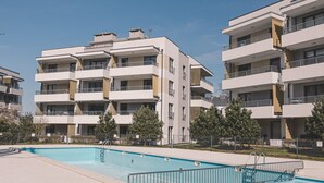 A modern apartment building with a swimming pool, balconies, and a clear sky.