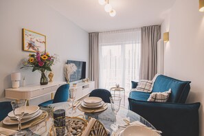 A modern living room with a dining area, a TV, and a large window with curtains.