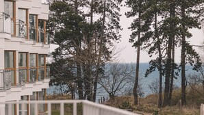 A modern building with large windows, a balcony, and a view of tall trees and a body of water.