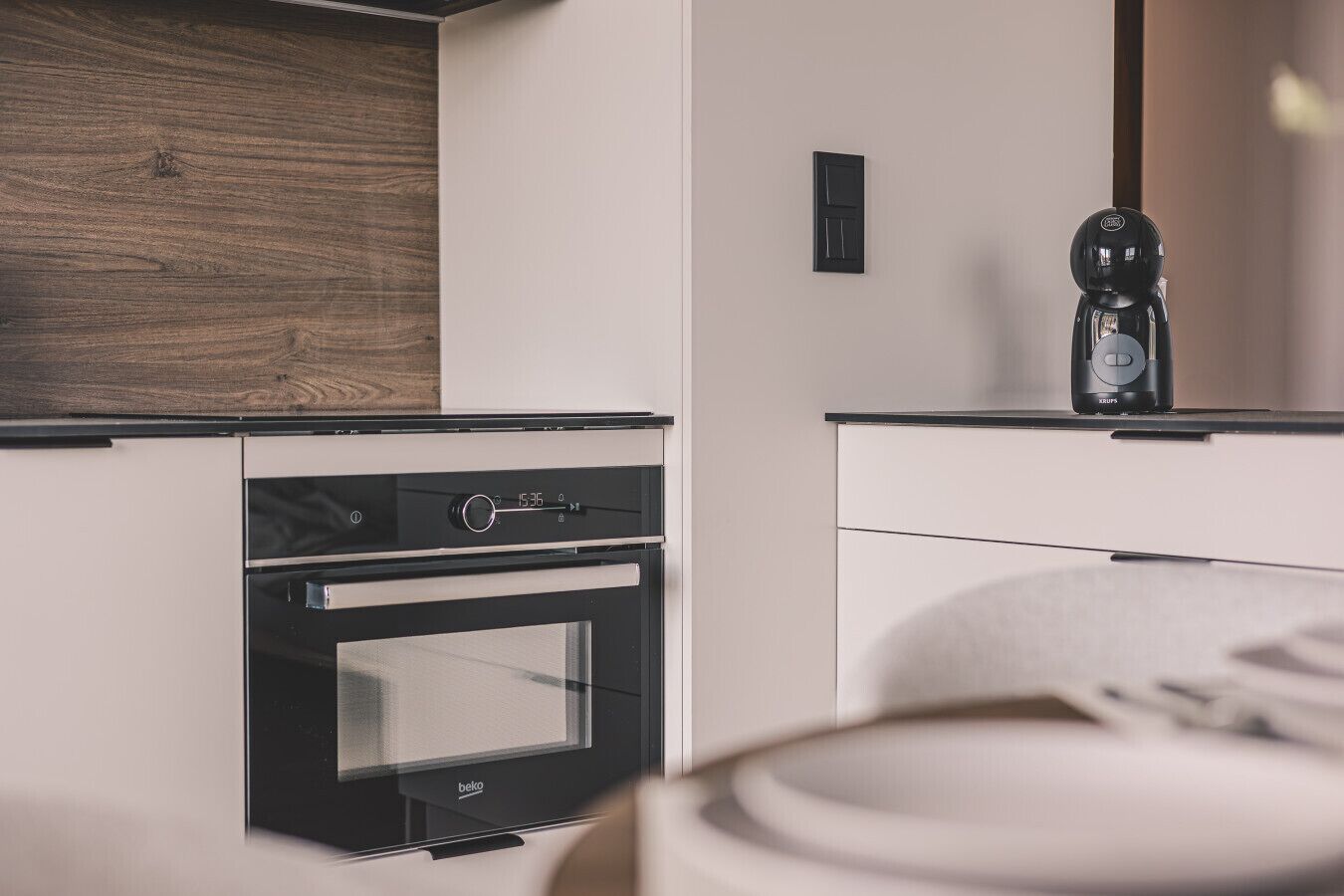 A modern kitchen with a built-in oven, a coffee machine, and a wooden backsplash.