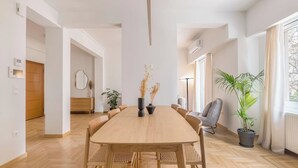A spacious room with a large wooden dining table surrounded by chairs, a potted plant, and a large window providing natural light. - Chic & Spacious 3BR Apartment at National Museum (Athina)