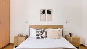 A neatly made bed with a striped bedspread, two bedside tables with lamps, and a pair of abstract art pieces on the wall. - Chic & Spacious 3BR Apartment at National Museum (Athina)