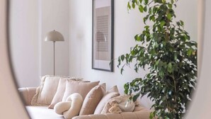 A living room with a beige sofa, a floor lamp, a framed picture on the wall, and a potted plant.