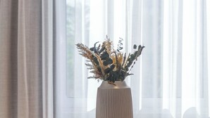 A dining area with a wooden table, a vase with dried plants, and a pink chair. - Monastiraki Living: Deluxe 2BR Apartment (Athens)