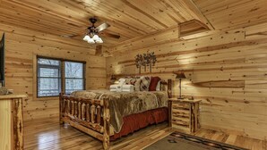 A log cabin bedroom with a wooden bed, a ceiling fan, a window, and a nightstand.