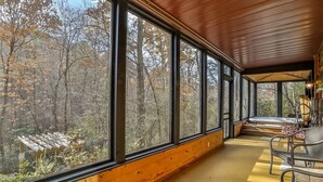 A covered porch with large windows, wooden walls, and outdoor seating.