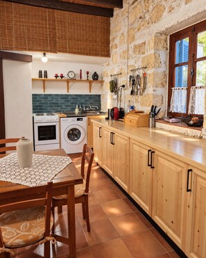 Una cocina con pared de piedra, armarios de madera, lavadora y comedor con mesa y sillas.