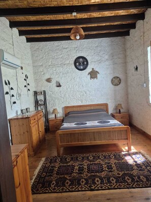 A rustic bedroom with a wooden bed, a woven rug, a wall clock, and a ceiling fan.