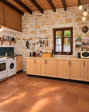 Cozinha com paredes de pedra, armários de madeira, máquina de lavar e utensílios pendurados.