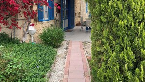 A traditional stone building with blue shutters and a red flowered tree in the foreground.