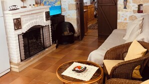 A living room with a fireplace, a wicker sofa, a small round table, and a stone wall.