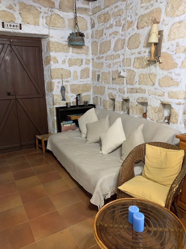 Una habitación acogedora con pared de piedra, armario de madera, sofá con cojines, sillón de mimbre y mesa de vidrio con velas.