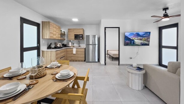 Una cocina moderna con armarios de madera, un refrigerador de acero inoxidable y un comedor con una mesa y sillas de madera.