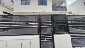 Ein modernes, zweistöckiges Haus mit weißer Fassade, einem Balkon im oberen Geschoss und einem schwarzen Metallzaun im Vordergrund.